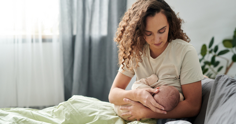 A woman sitting on the bed breastfeeding her baby.