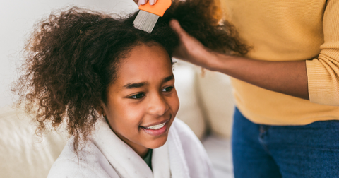 A young black girl having her hair lice combed by her mom.