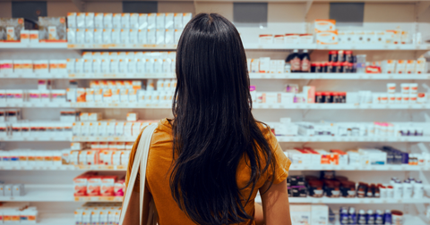 A woman standing in front of a shelf filled with over the counter treatments for head lice.
