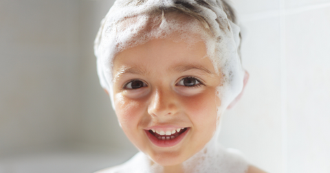 A little boy in the bath using natural lice shampoo by Hair Fairies.