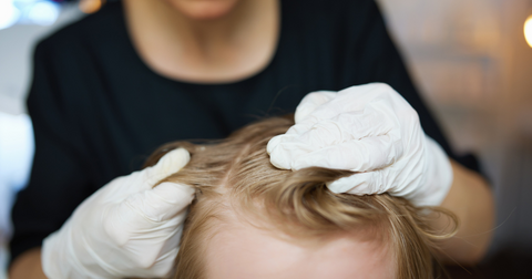 A woman in white gloves looks through a girl's hair for lice.