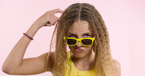 Young girl wearing yellow sunglasses and dress scratching her head because of lice.