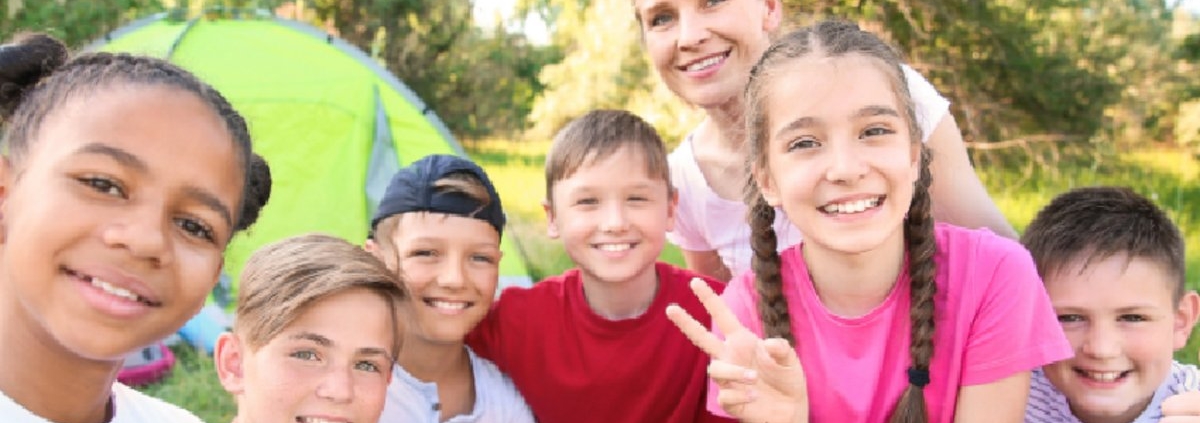 A group of smiling children and an adult gathered outdoors near a tent.