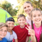 A group of smiling children and an adult gathered outdoors near a tent.