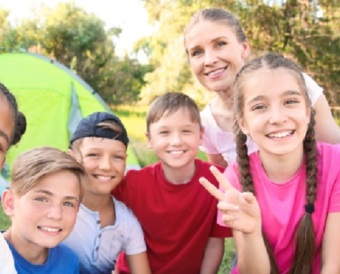 A group of smiling children and an adult gathered outdoors near a tent.