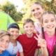 A group of smiling children and an adult gathered outdoors near a tent.