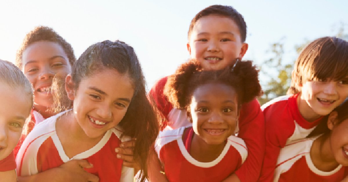 A group of children in matching team shirts smiling outdoors.