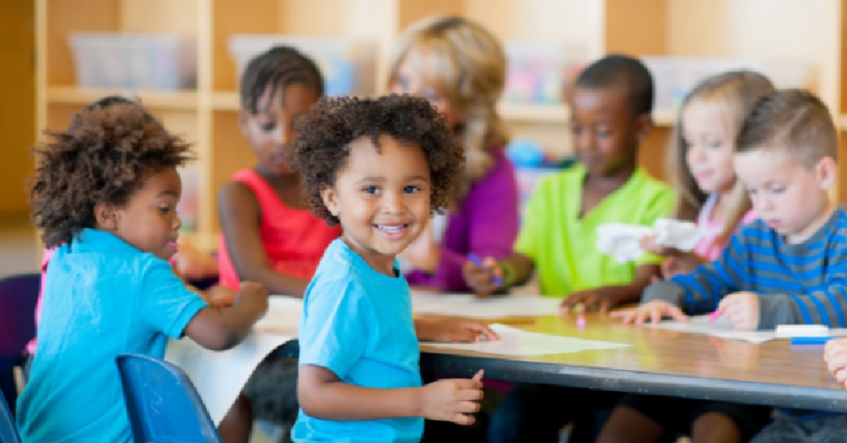 Young children and a teacher engaged in classroom activities, with students drawing and learning together.