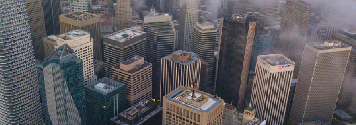 Aerial view of a dense San Francisco cityscape with high-rise buildings partially covered by low clouds and fog.