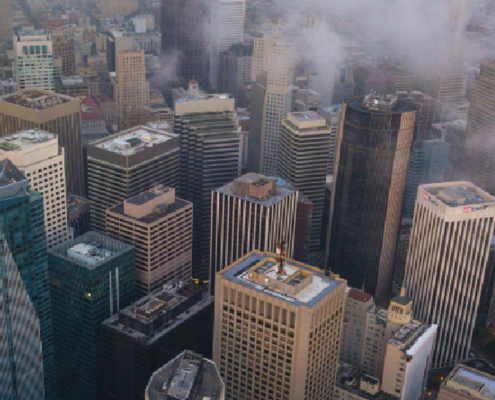 Aerial view of a dense San Francisco cityscape with high-rise buildings partially covered by low clouds and fog.