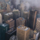Aerial view of a dense San Francisco cityscape with high-rise buildings partially covered by low clouds and fog.