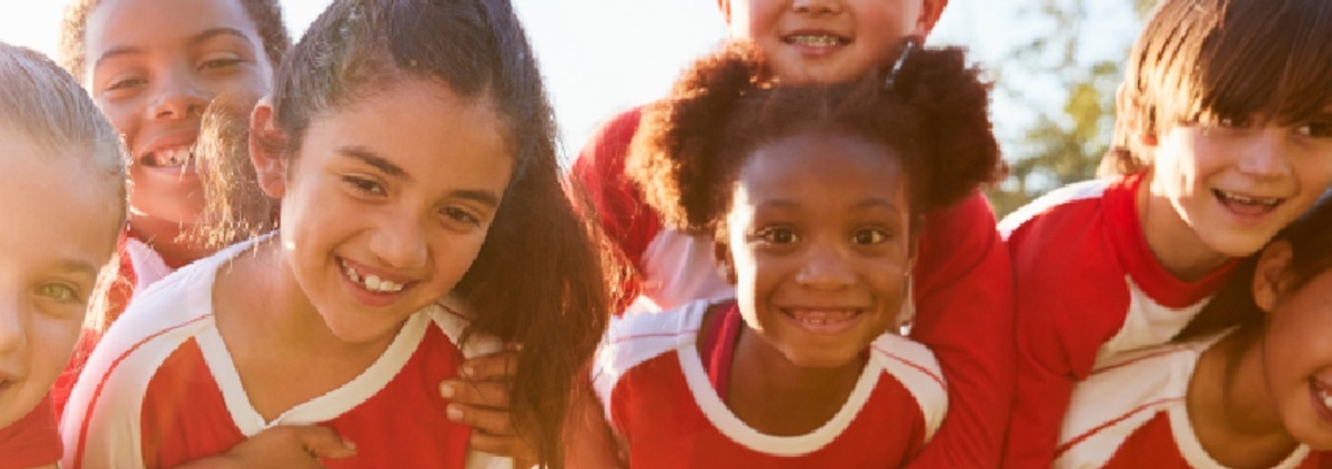 Young athletes in red and white sports jerseys huddle closely together and smile outdoors before a team game.