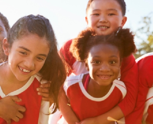 Young athletes in red and white sports jerseys huddle closely together and smile outdoors before a team game.